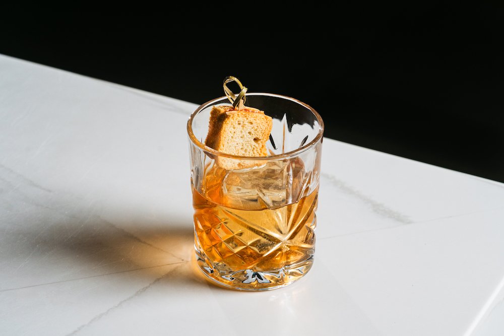 Cóctel Preserving Traditions de American Social, servido en vaso corto con hielo y coronado con mini sándwich PB&J.
