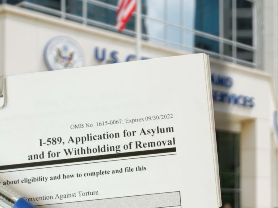 Montaje de formulario de solicitud de asilo con edificio de USCIS de fondo.